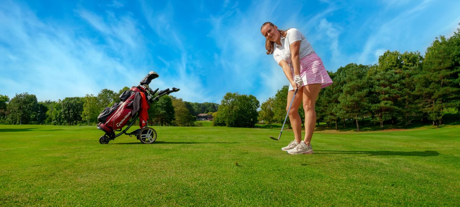 Female golfer chipping towards the camera on a golf course in Woking