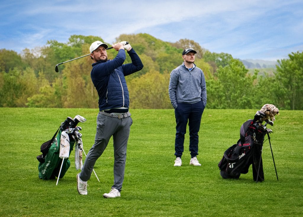 Man hitting a golf ball at a golf course in Woking while another player watches behind