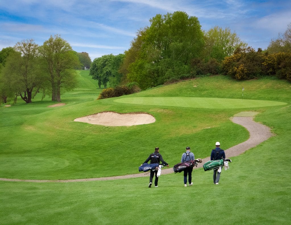 Three golfers walking towards a golf hole on a golf course in Surrey