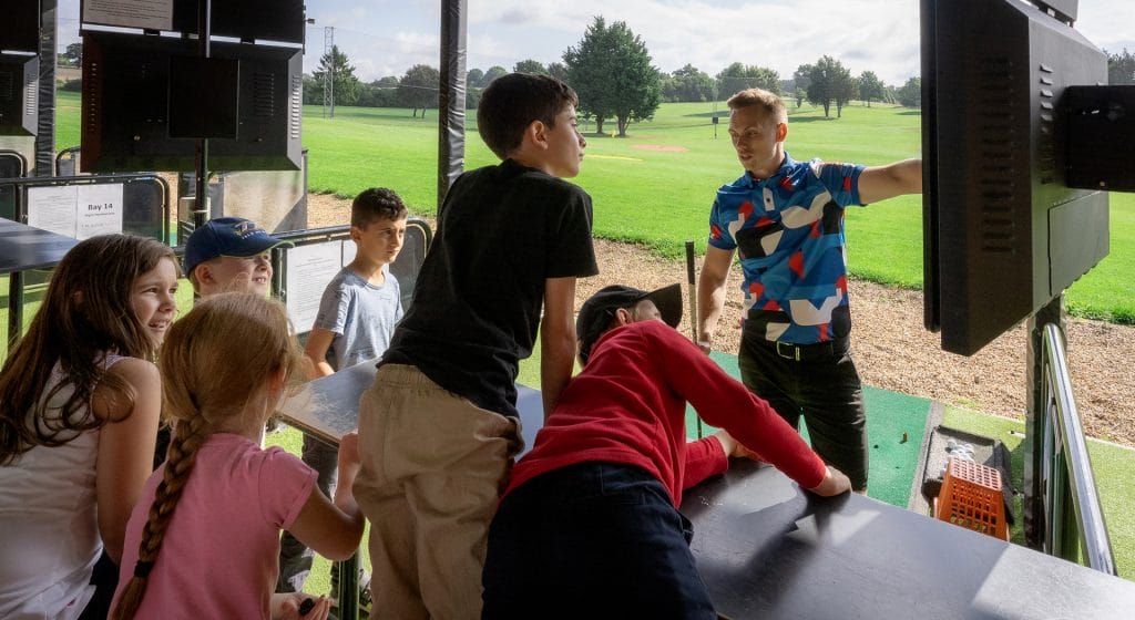 golf coach instructing a kids golf lesson in woking on the driving range