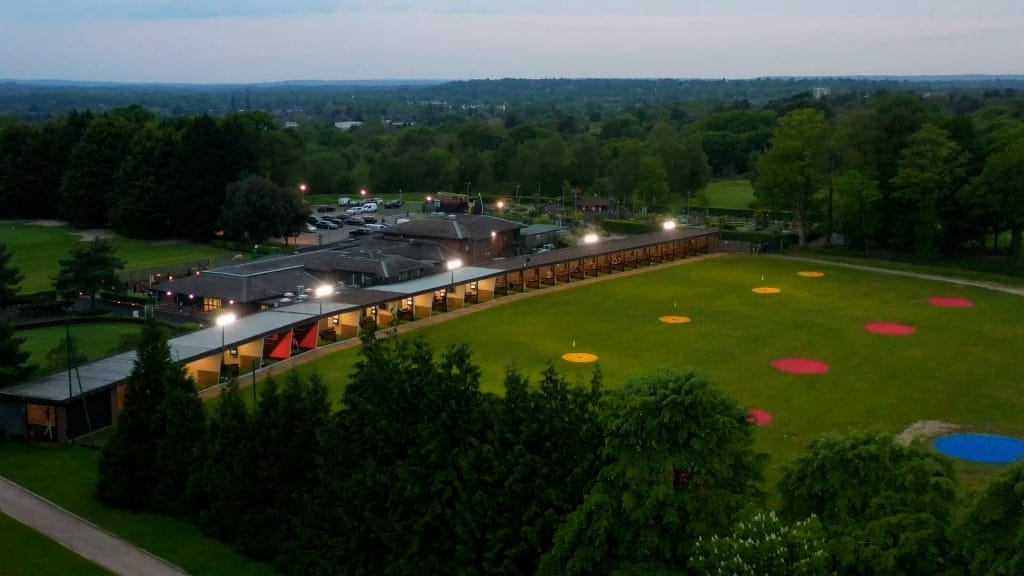 Floodlit golf driving range in Surrey seen from above, offering virtual golf and evening practice.